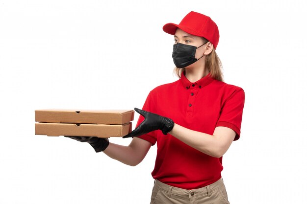Une vue de face femme courrier en chemise rouge bonnet rouge gants noirs et masque noir livrant des boîtes de pizza