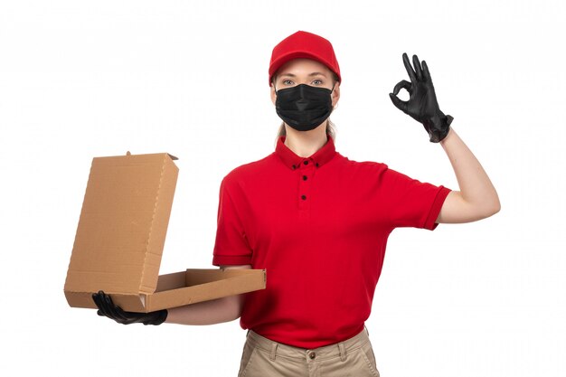 Une vue de face femme courrier en chemise rouge bonnet rouge gants noirs et masque noir tenant une boîte à pizza vide