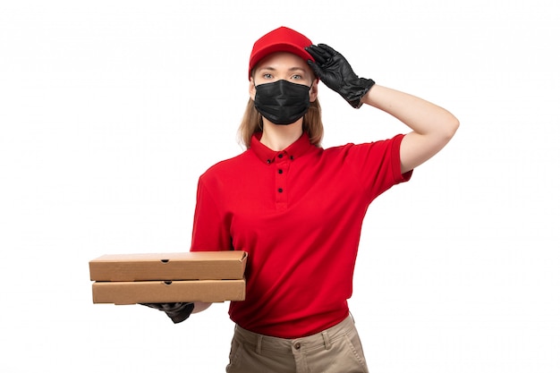 Une vue de face femme courrier en chemise rouge bonnet rouge gants noirs et masque noir tenant des boîtes à pizza sur blanc