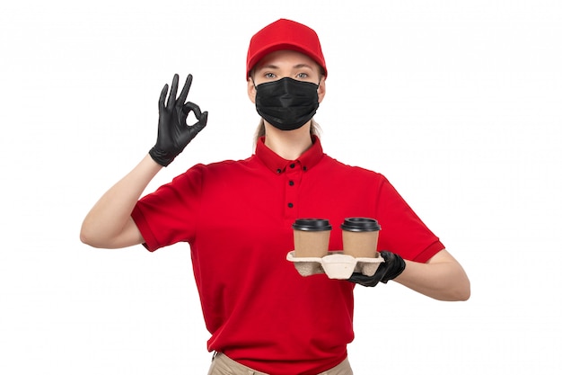 Une vue de face femme courrier en chemise rouge bonnet rouge gants noirs et masque noir tenant du café