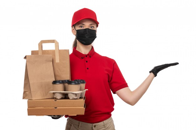 Une vue de face femme courrier en chemise rouge bonnet rouge gants noirs et masque noir tenant des emballages alimentaires et du café sur blanc
