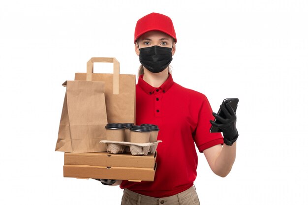 Une vue de face femme courrier en chemise rouge bonnet rouge gants noirs et masque noir tenant des paquets de café et smartphone