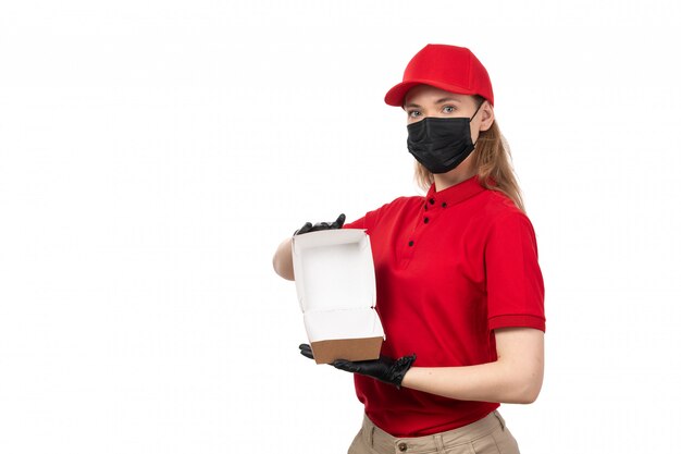 Une vue de face femme courrier en chemise rouge gants capblack rouge et masque noir tenant un paquet alimentaire vide sur blanc