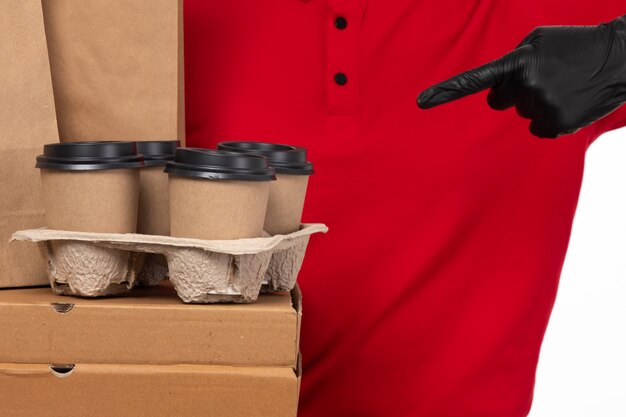 Une vue de face femme courrier en chemise rouge gants noirs tenant des boîtes et des tasses à café