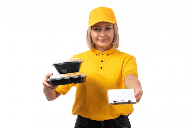 Une vue de face femme courrier jeune en chemise jaune casquette jaune et jean noir tenant des bols avec de la nourriture et le bloc-notes de signature sur l'uniforme blanc