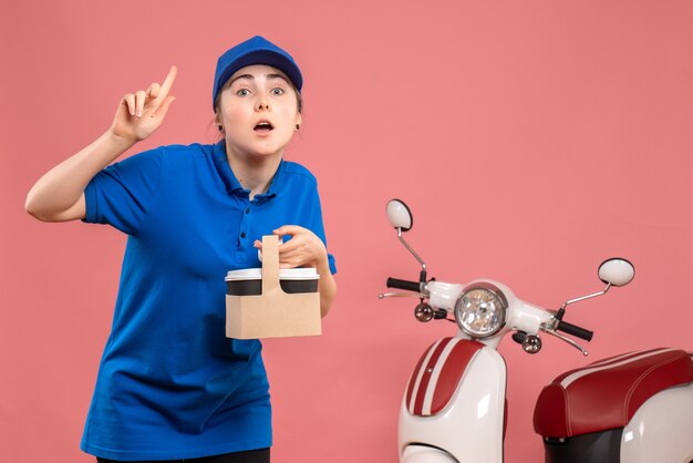 Vue de face femme courrier avec livraison de café sur le service de livraison de travail rose travail travailleur femme vélo uniforme