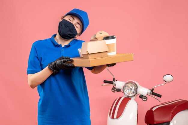 Vue de face femme courrier en masque avec livraison de café et de nourriture sur le rose