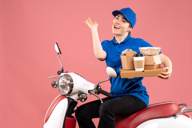 Vue de face femme courrier avec des paquets de nourriture et des boîtes sur le service d'uniforme de vélo de livraison de nourriture de couleur rose