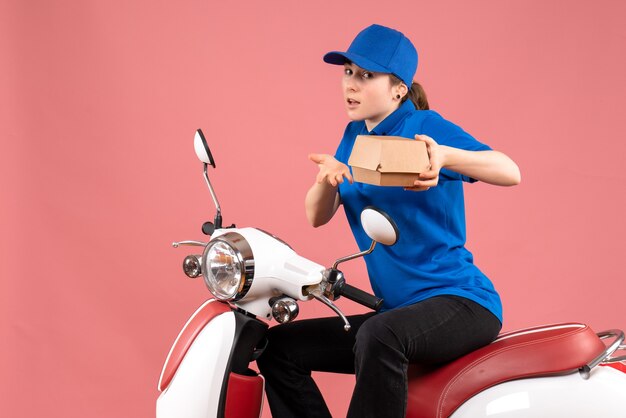 Vue de face femme courrier avec petit paquet de nourriture sur un vélo de livraison de nourriture de travailleur uniforme de couleur rose