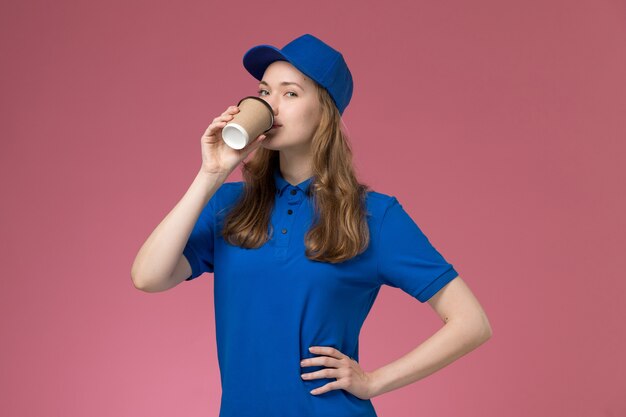 Vue de face femme courrier en uniforme bleu boire du café sur l'uniforme de service de bureau rose offrant un travail de l'entreprise