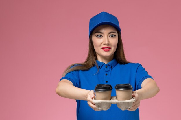 Vue de face femme courrier en uniforme bleu et cape offrant des tasses à café sur mur rose