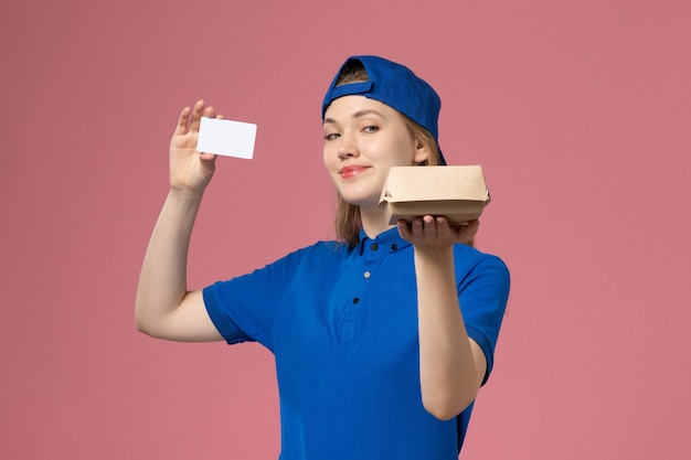 Vue de face femme courrier en uniforme bleu et cape tenant peu de colis de nourriture de livraison avec carte sur le mur rose, employé du service de livraison des travailleurs