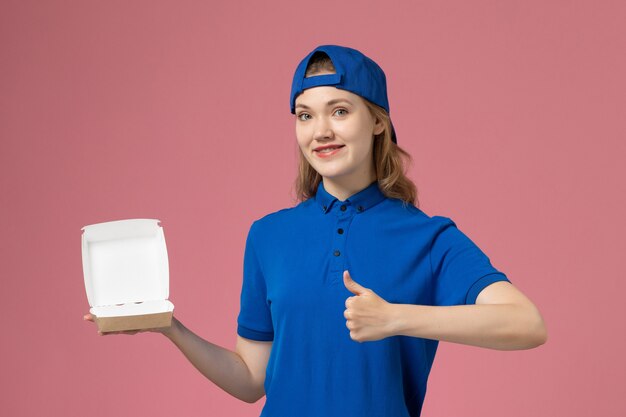 Vue de face femme courrier en uniforme bleu et cape tenant peu de colis de nourriture de livraison sur le mur rose, service uniforme de livraison employé employé