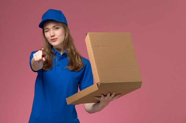 Vue de face femme courrier en uniforme bleu tenant la boîte de livraison de nourriture un clin de œil sur le travail de l'entreprise uniforme de bureau rose