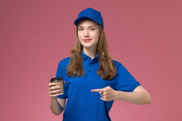 Photo gratuite vue de face femme courrier en uniforme bleu tenant une tasse de café marron sur fond rose uniforme de service offrant un travail de l'entreprise