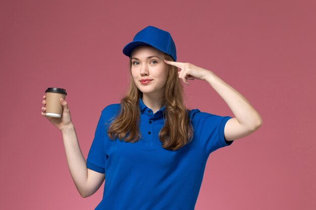 Vue de face femme courrier en uniforme bleu tenant une tasse de café marron avec un léger sourire sur l'uniforme de travail de service de bureau rose clair entreprise de livraison