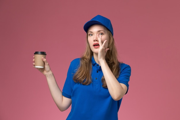 Vue de face femme courrier en uniforme bleu tenant une tasse de café marron sur un travail de travail uniforme de service de bureau rose clair entreprise de livraison