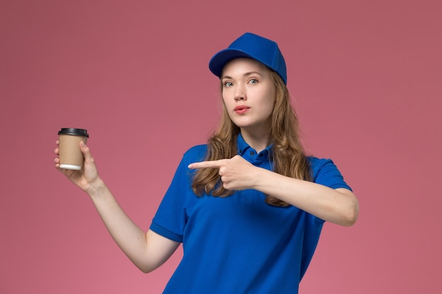 Vue de face femme courrier en uniforme bleu tenant une tasse de café marron sur un uniforme de travail de bureau rose clair entreprise de livraison