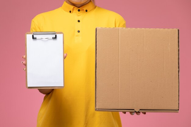 Vue de face femme courrier en uniforme jaune cape jaune tenant le bloc-notes paquet alimentaire sur le bureau rose livraison uniforme couleur de travail féminin