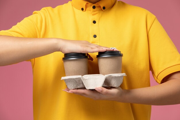 Photo gratuite vue de face femme courrier en uniforme jaune cape jaune tenant le café sur le fond rose travail de livraison uniforme couleur de travail