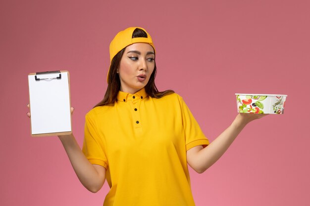 Vue de face femme courrier en uniforme jaune et cape tenant un bol de livraison rond avec bloc-notes sur le mur rose service de livraison uniforme fille travailleur