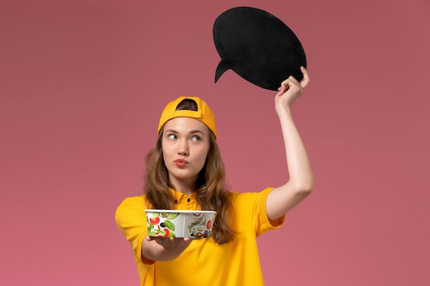 Vue de face femme courrier en uniforme jaune et cape tenant une pancarte noire avec bol sur le mur rose de l'entreprise d'uniforme de livraison de services