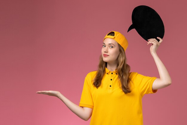 Vue de face femme courrier en uniforme jaune et cape tenant une pancarte noire sur le mur rose entreprise d'uniforme de livraison de services