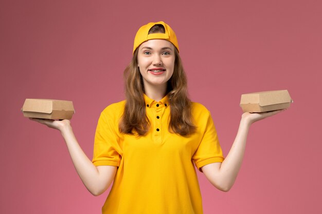 Vue de face femme courrier en uniforme jaune et cape tenant peu de colis alimentaires de livraison sur le mur rose service travail travail de livraison uniforme