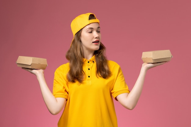 Vue de face femme courrier en uniforme jaune et cape tenant peu de colis alimentaires de livraison sur le mur rose uniforme de travail de livraison de travailleur de service