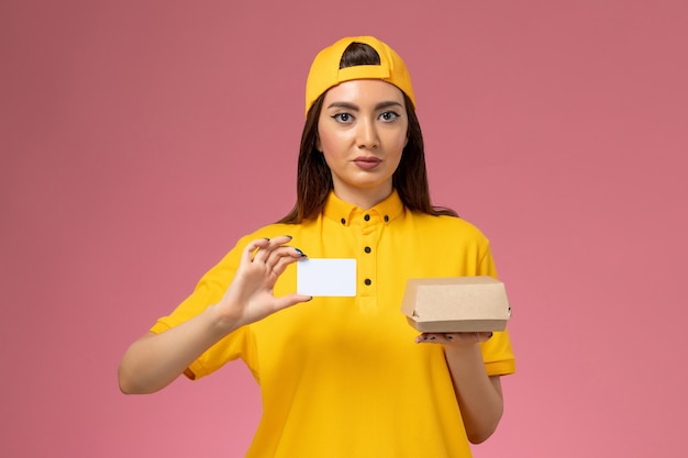 Vue De Face Femme Courrier En Uniforme Jaune Et Cape Tenant Peu De Colis De Nourriture De Livraison Et Carte Sur Mur Rose Clair Service De Livraison Uniforme De Travail De Travailleur De L'entreprise