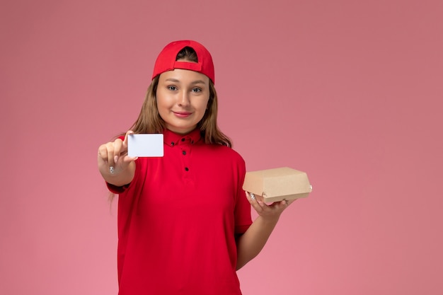 Vue de face femme courrier en uniforme rouge et cape tenant peu de colis de nourriture de livraison et carte sur mur rose, travail de service de livreur uniforme