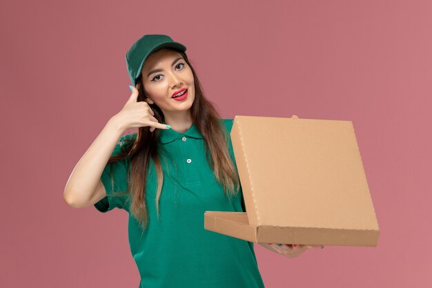 Vue de face femme courrier en uniforme vert tenant la boîte de livraison de nourriture sur le mur rose entreprise service de livraison uniforme de travail