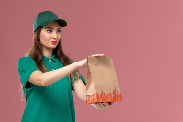 Vue de face femme courrier en uniforme vert tenant un paquet de papier alimentaire sur le mur rose clair service de livraison uniforme