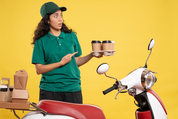 Vue de face femme coursier en uniforme vert avec café sur fond jaune couleur service travailleur travail travail nourriture femme