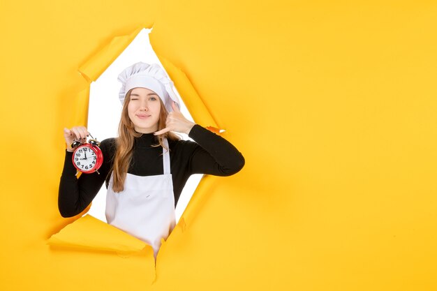 Vue de face femme cuisinier en casquette de cuisinier blanc tenant une horloge sur une photo jaune couleur travail cuisine soleil nourriture émotion