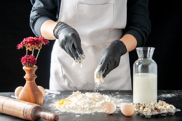 Vue de face femme cuisinier casser les œufs en farine sur un travail sombre pâtisserie tarte boulangerie cuisson gâteau biscuit pâte cuire