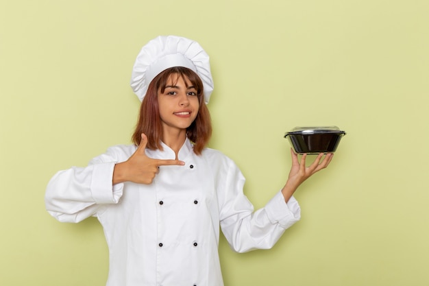 Photo gratuite vue de face femme cuisinier en costume de cuisinier blanc tenant un bol sur une surface vert clair