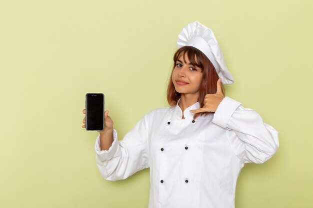 Vue de face femme cuisinier en costume de cuisinier blanc tenant son smartphone sur un bureau vert