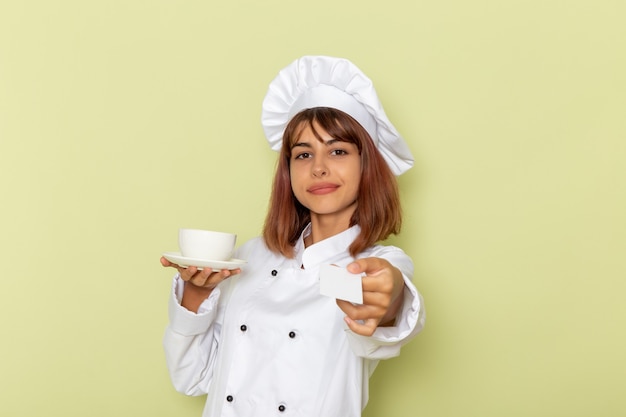 Vue De Face Femme Cuisinier En Costume De Cuisinier Blanc Tenant Une Tasse De Thé Et Une Carte Sur La Surface Verte