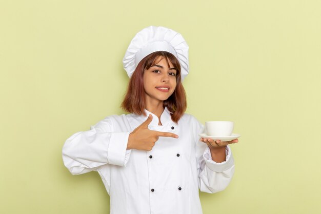 Vue de face femme cuisinier en costume de cuisinier blanc tenant une tasse de thé sur une surface verte