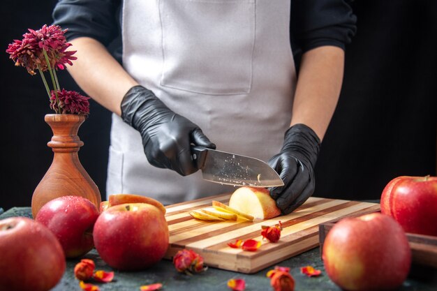 Vue de face femme cuisinier coupe des pommes sur un régime de légumes sombres repas salade de fruits exotiques