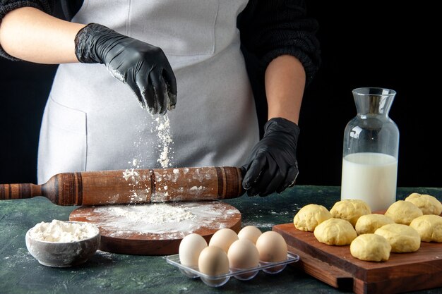 Vue de face femme cuisinier étaler la pâte avec de la farine sur un travail sombre cuisine hotcake pâte crue cuire au gâteau tarte oeuf de travailleur