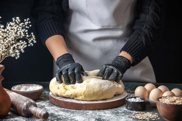 Vue de face femme cuisinier étaler la pâte sur le travail de pâtisserie sombre pâte crue four à tarte boulangerie hotcake