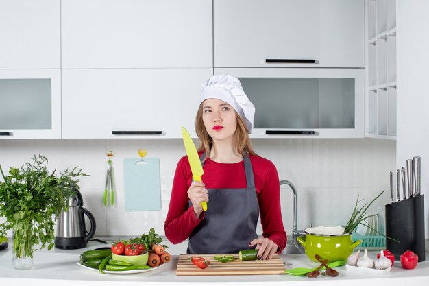 Vue de face femme cuisinier réfléchie en tablier tenant un couteau