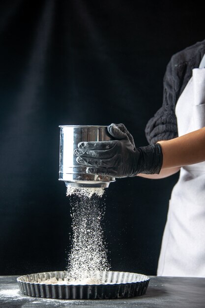 Vue de face femme cuisinier semant de la farine blanche dans une casserole sur un travail de pâtisserie sombre gâteau aux œufs tarte à la cuisine des travailleurs de la boulangerie