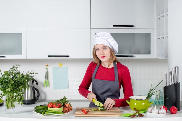 Vue de face femme cuisinier en tablier coupant le concombre tout en regardant à l'avant