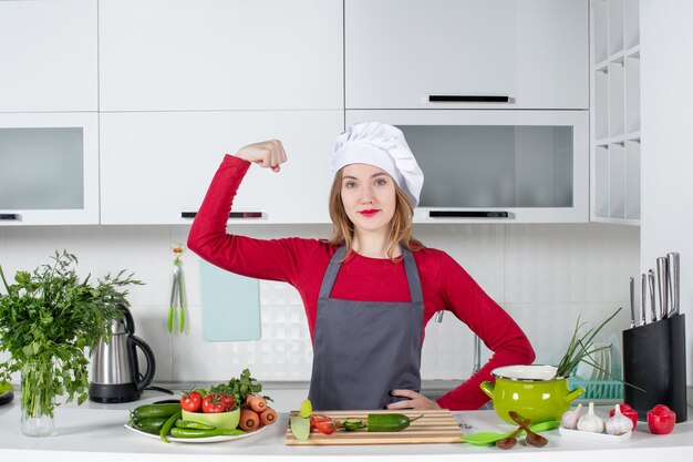 Vue de face femme cuisinier en tablier montrant ses muscles du bras