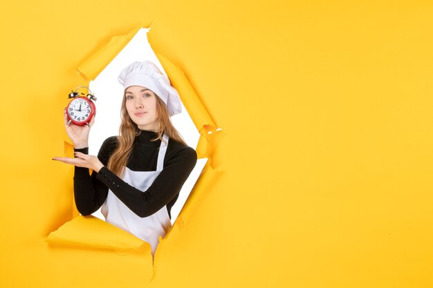 Vue de face femme cuisinier tenant des horloges sur la nourriture jaune photo couleur travail cuisine émotions temps soleil