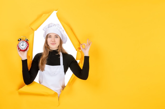 Photo gratuite vue de face femme cuisinier tenant des horloges sur le temps jaune nourriture photo travail émotion soleil cuisine couleur