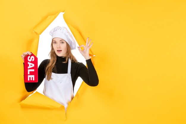 Vue de face femme cuisinier tenant vente rouge écrit sur la couleur jaune travail cuisine émotion photo alimentaire